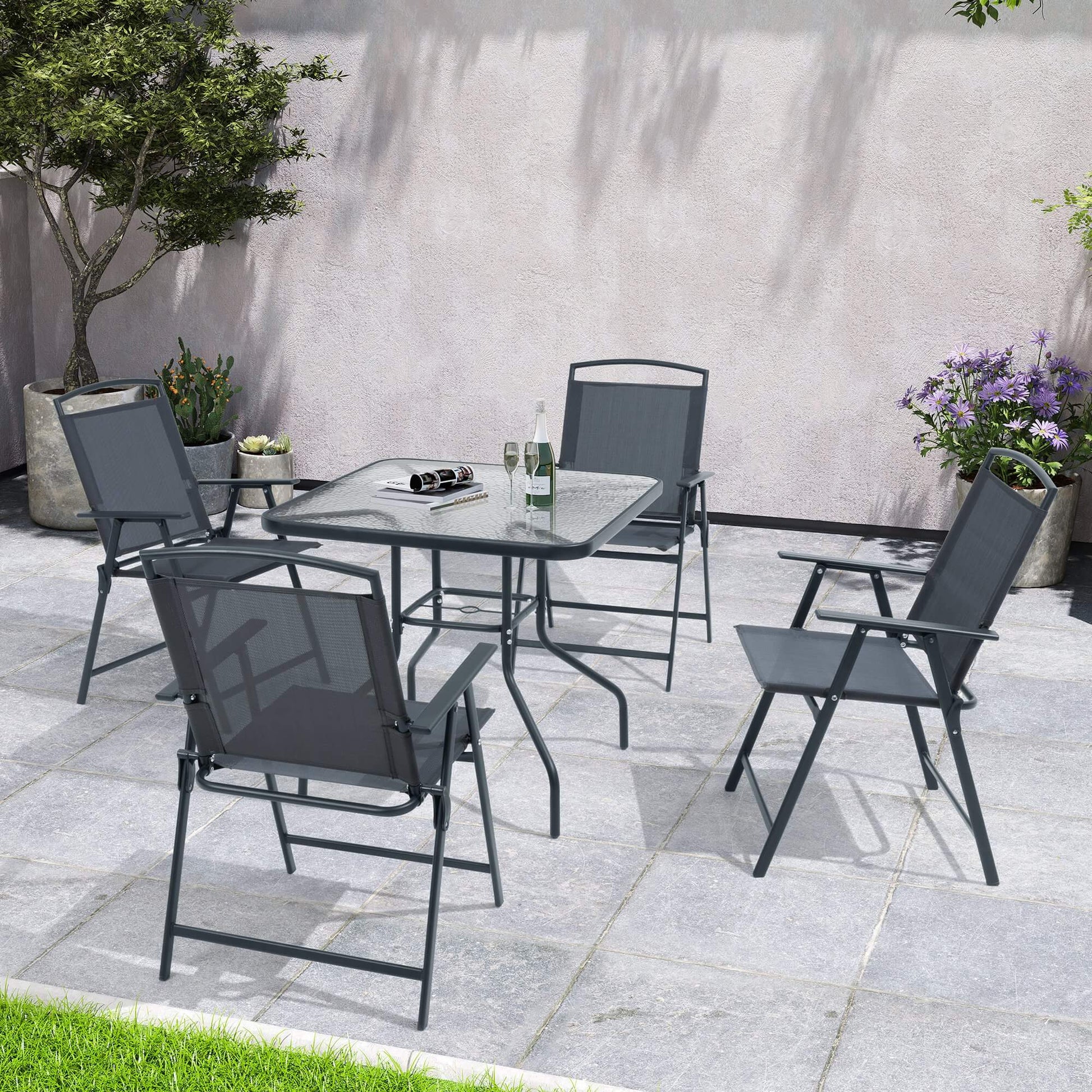 5-piece dark gray patio dining set with glass top table and 4 folding chairs on a stone patio.