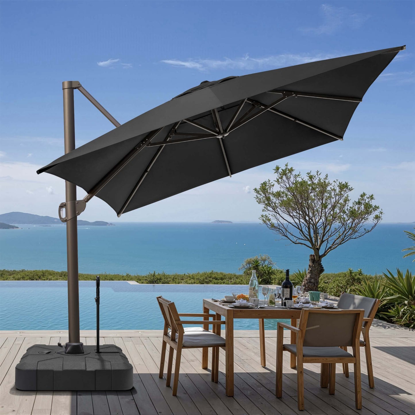 Tilted dark gray square cantilever patio umbrella on a rolling base with pull rod, shading an oceanfront dining set.