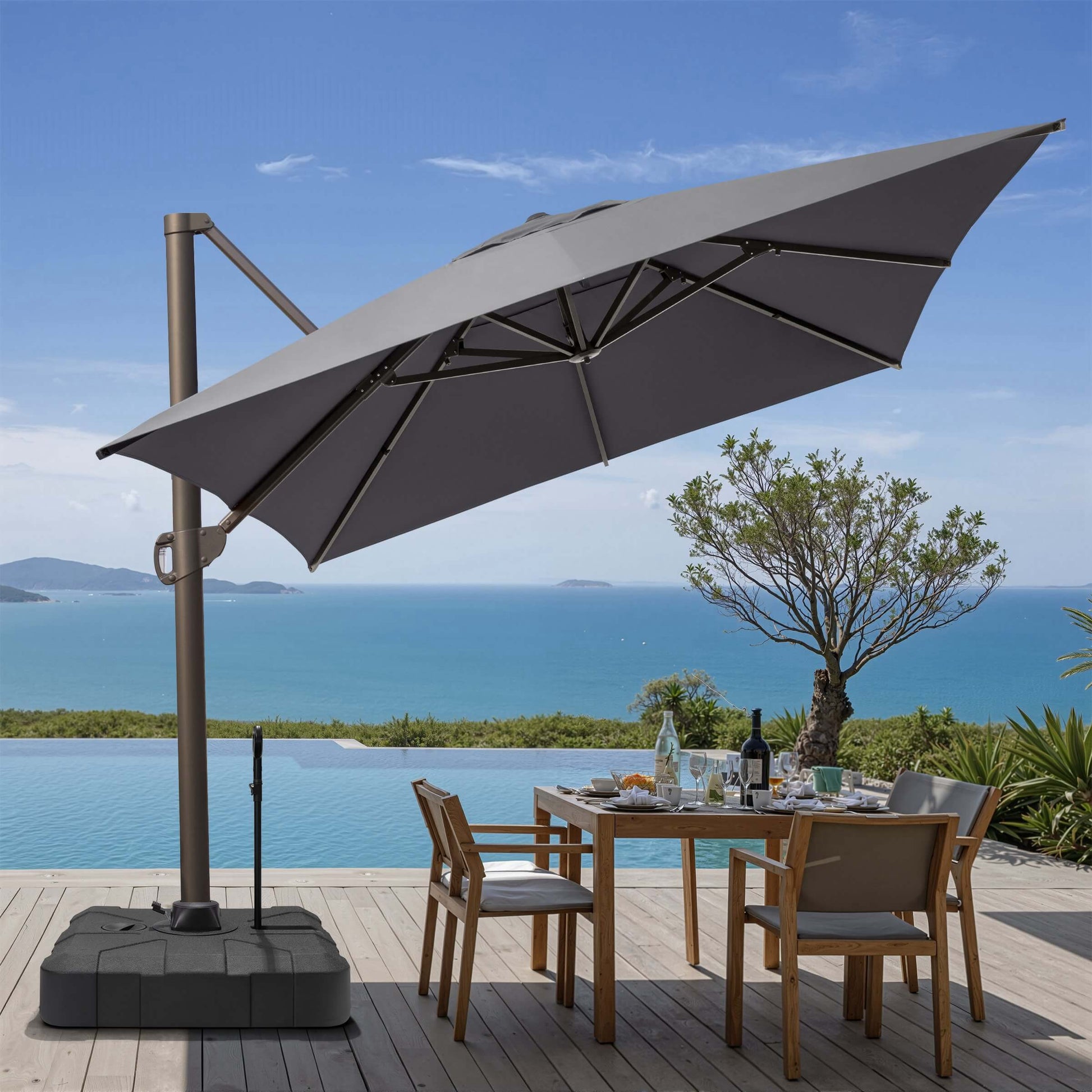 Tilted gray square cantilever patio umbrella on rolling base with pull rod, shading an oceanfront dining set.