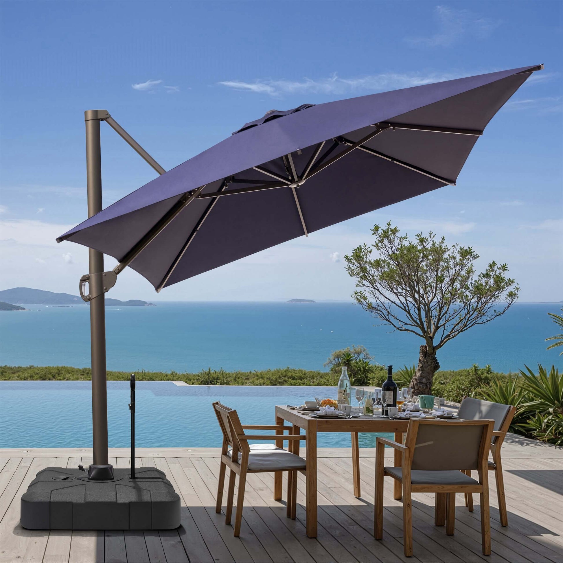 Tilted navy blue square cantilever patio umbrella on rolling base with pull rod, shading an oceanfront dining set.