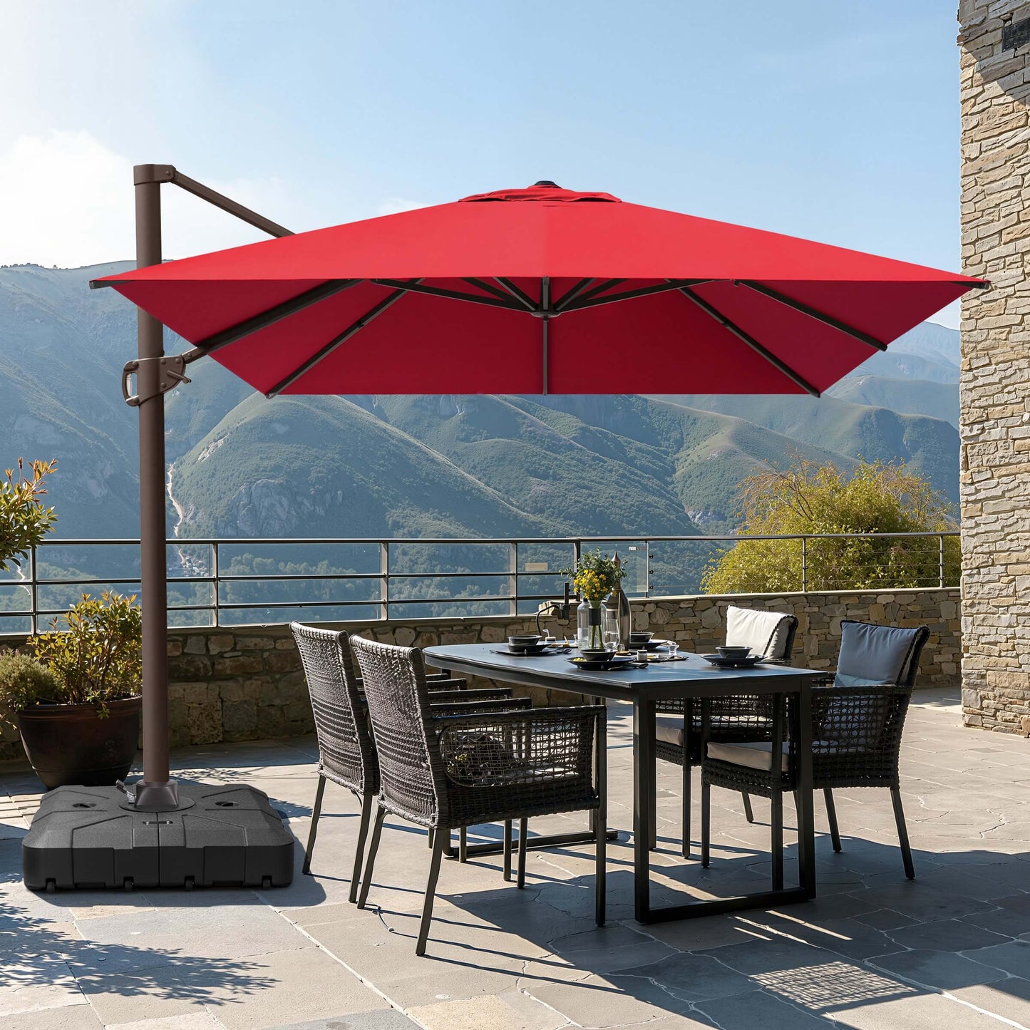 Red square cantilever patio umbrella with wheeled base shading a wicker dining set on a mountain terrace.
