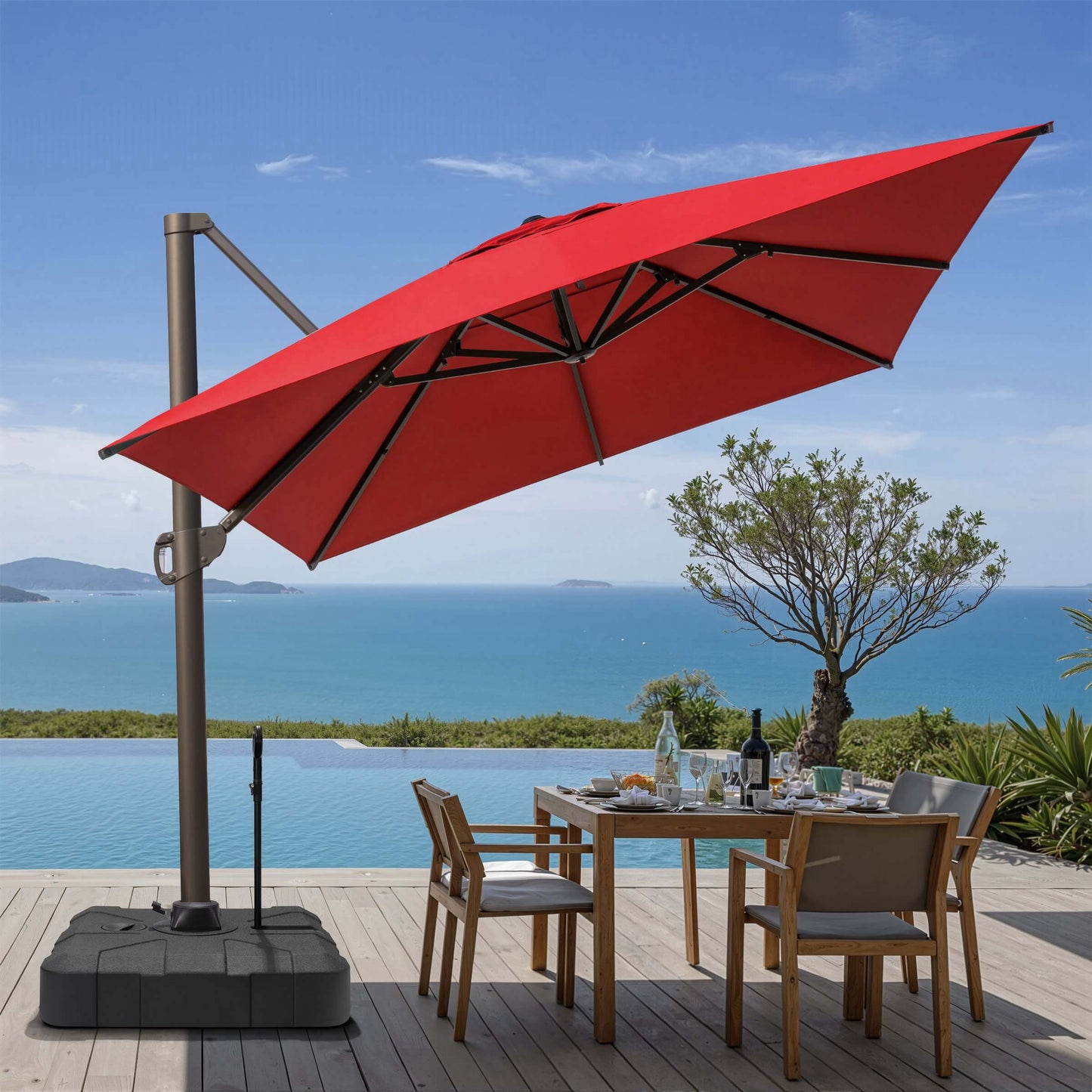 Tilted red square cantilever patio umbrella on rolling base with pull rod, shading an oceanfront dining set.