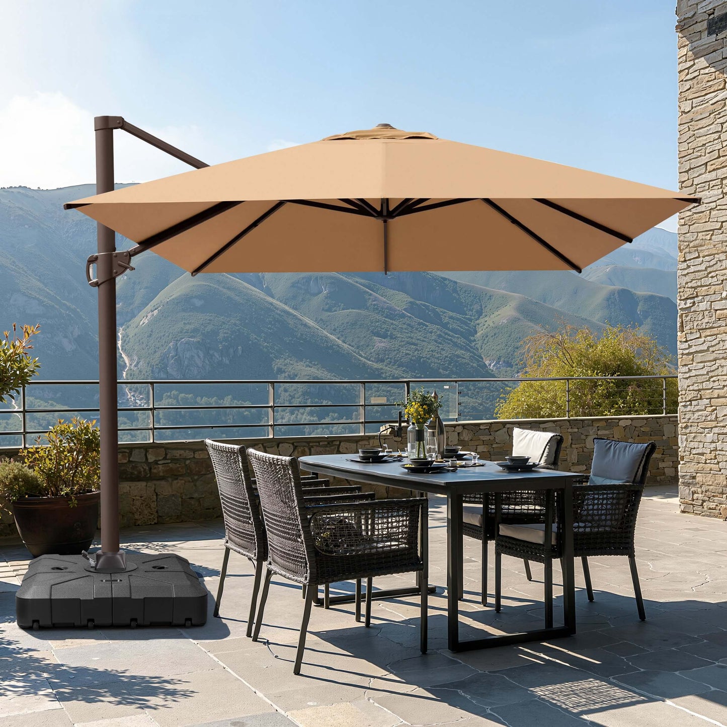 Tan square single-top cantilever patio umbrella with wheeled base shading an outdoor dining set on a scenic terrace.