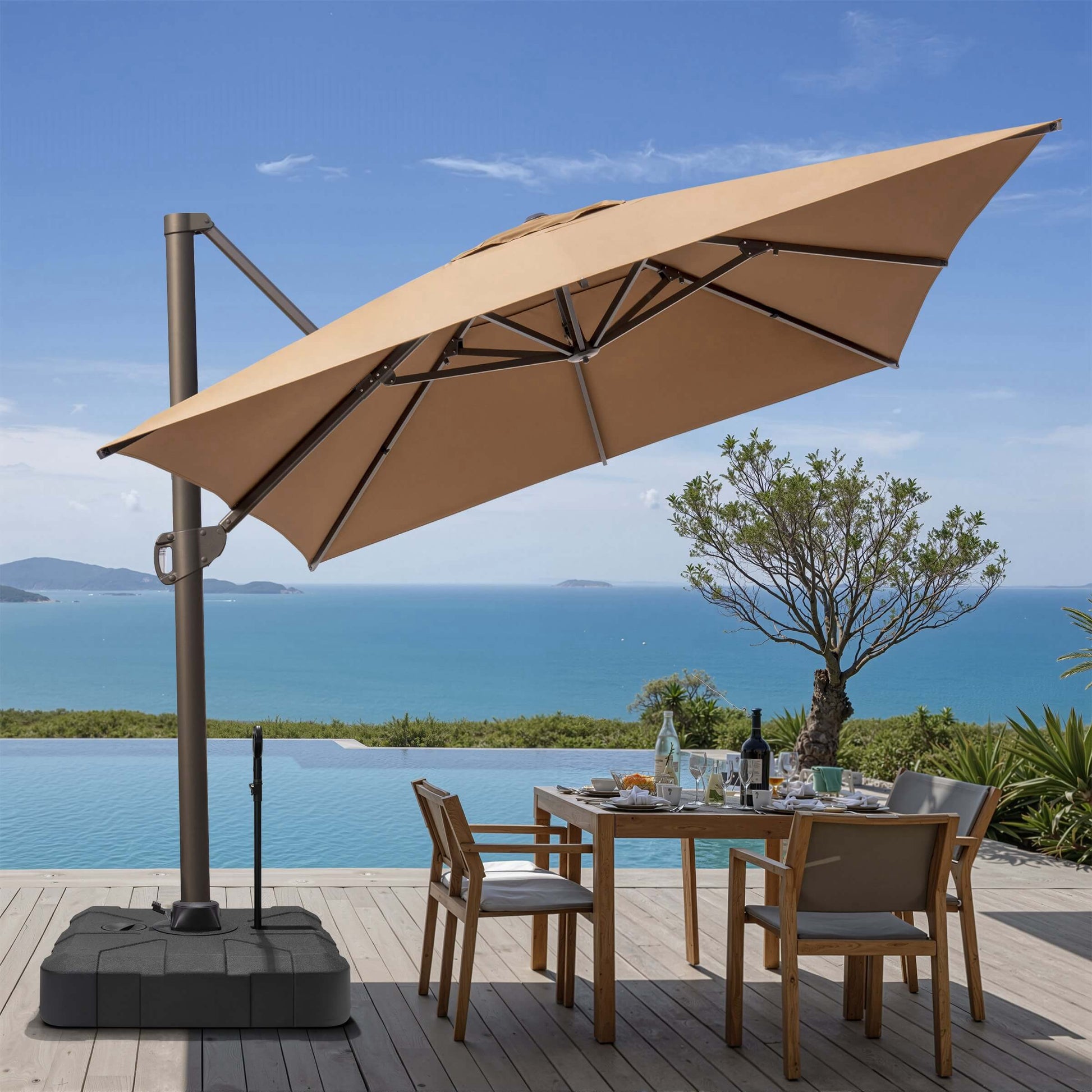 Tilted tan square cantilever patio umbrella on a rolling base with pull rod, shading an oceanfront dining set.