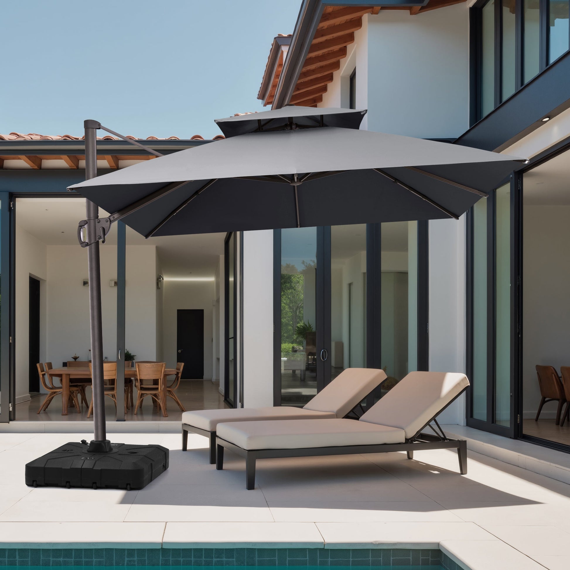 A charcoal grey 10x10 ft square cantilever patio umbrella with heavy-duty base shading chaise lounge chairs at a modern villa poolside