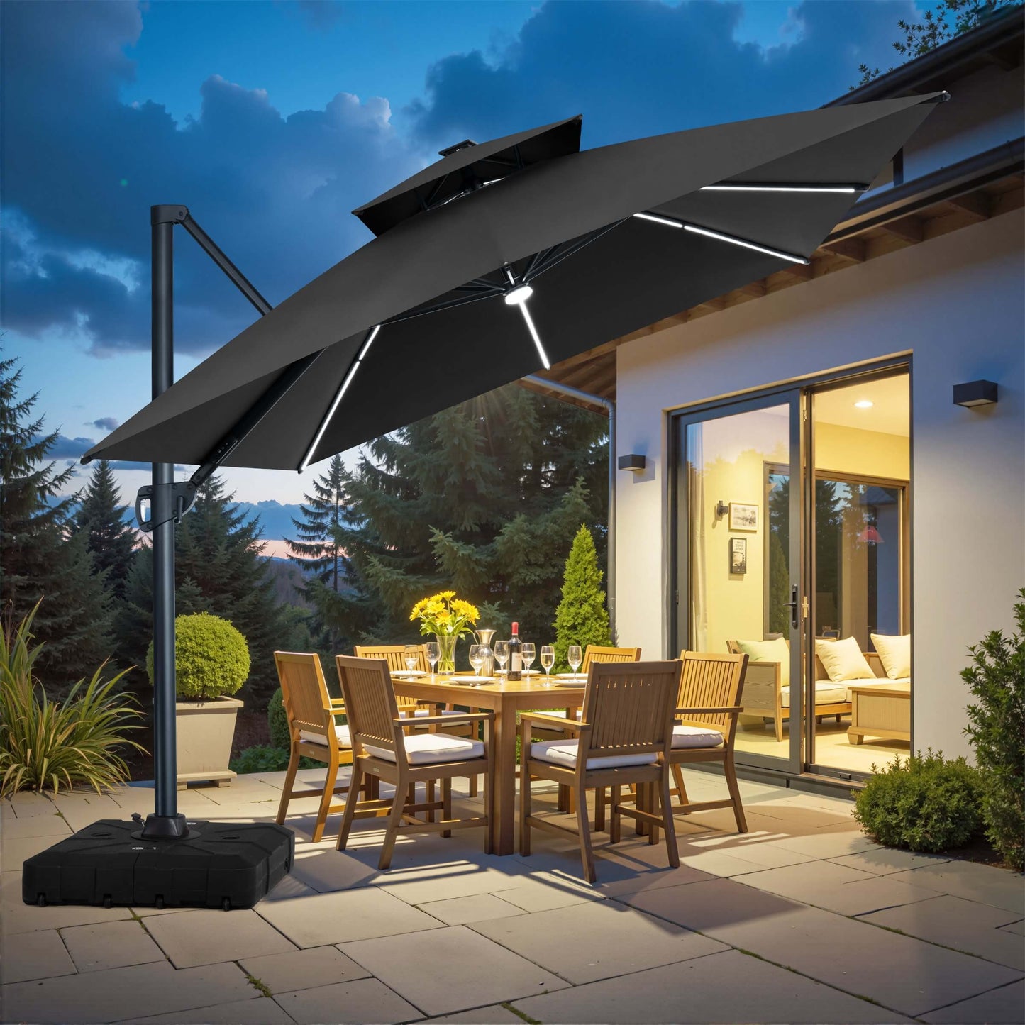 Black square double-top cantilever patio umbrella with LED lights and rolling base illuminating an evening outdoor dining area.