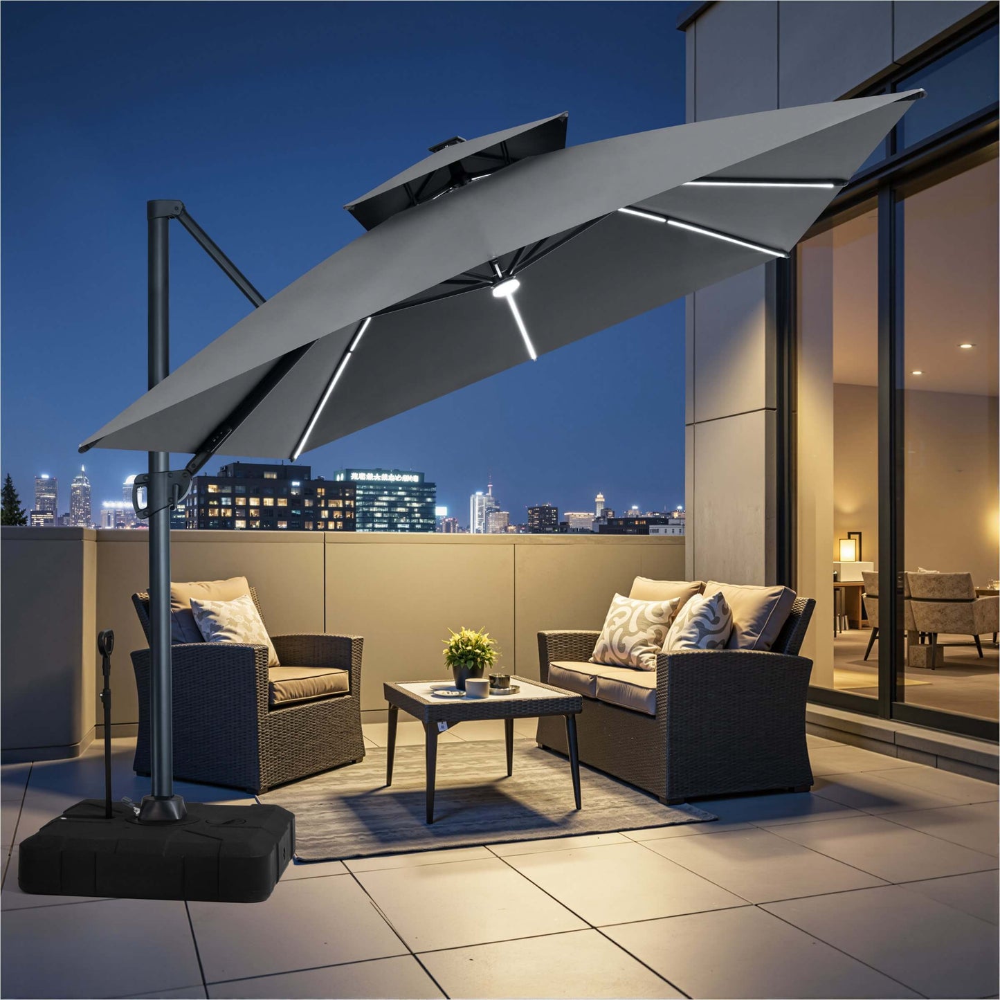 Grey square double-top LED cantilever patio umbrella with pull-rod wheeled base over balcony furniture at night.