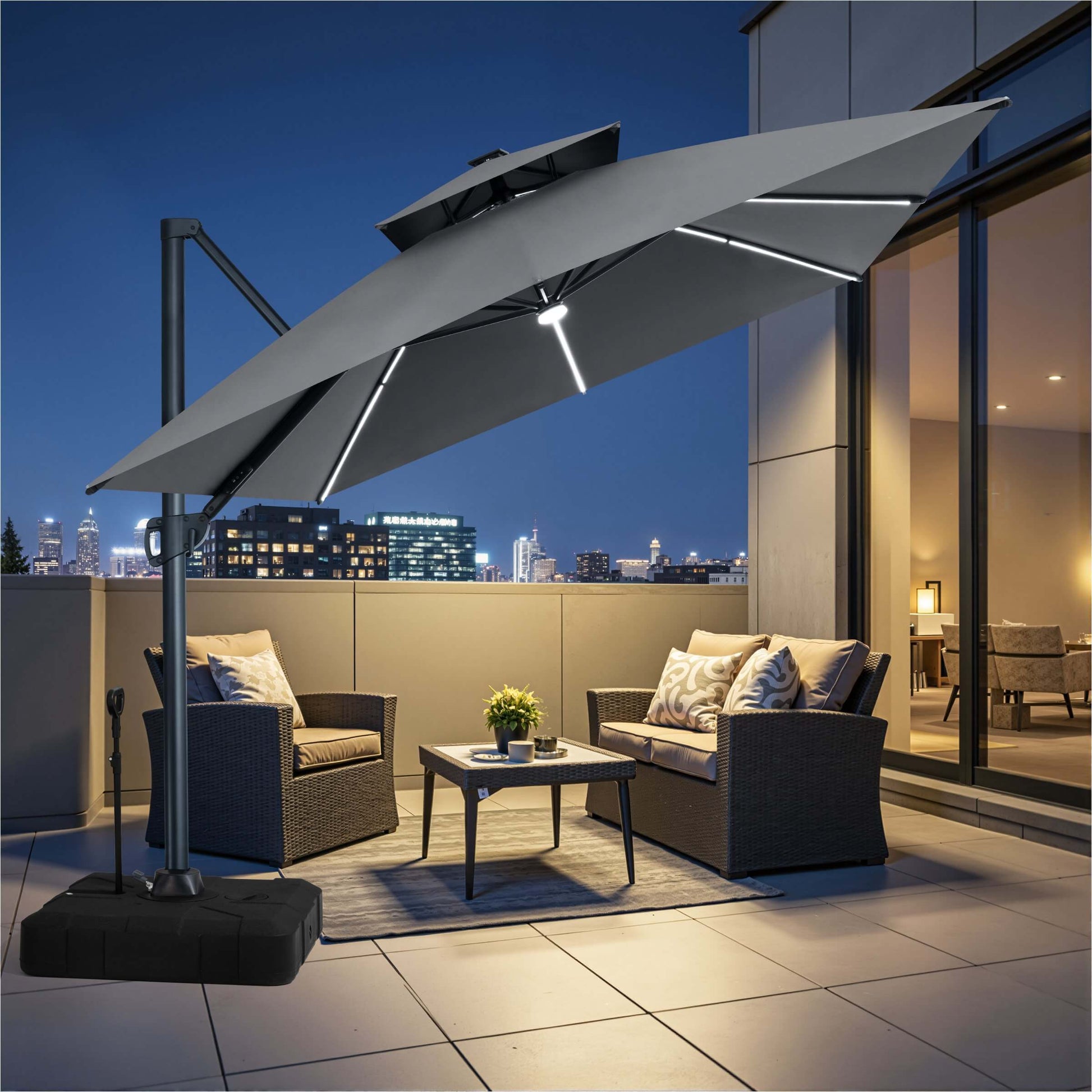 Grey square double-top LED cantilever patio umbrella with pull-rod wheeled base over balcony furniture at night.
