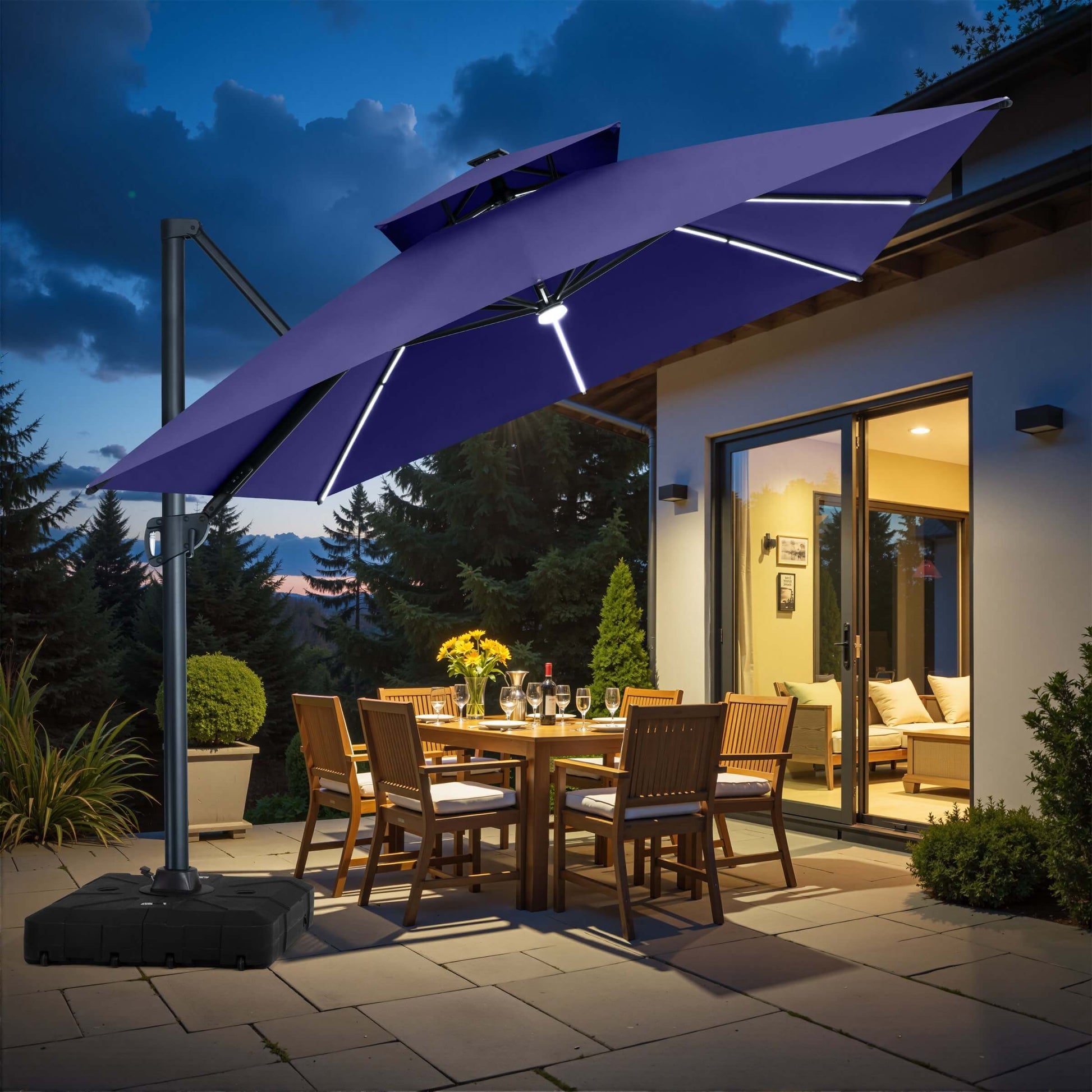 Navy blue square double-top LED cantilever umbrella with rolling base illuminating patio dining area at night.