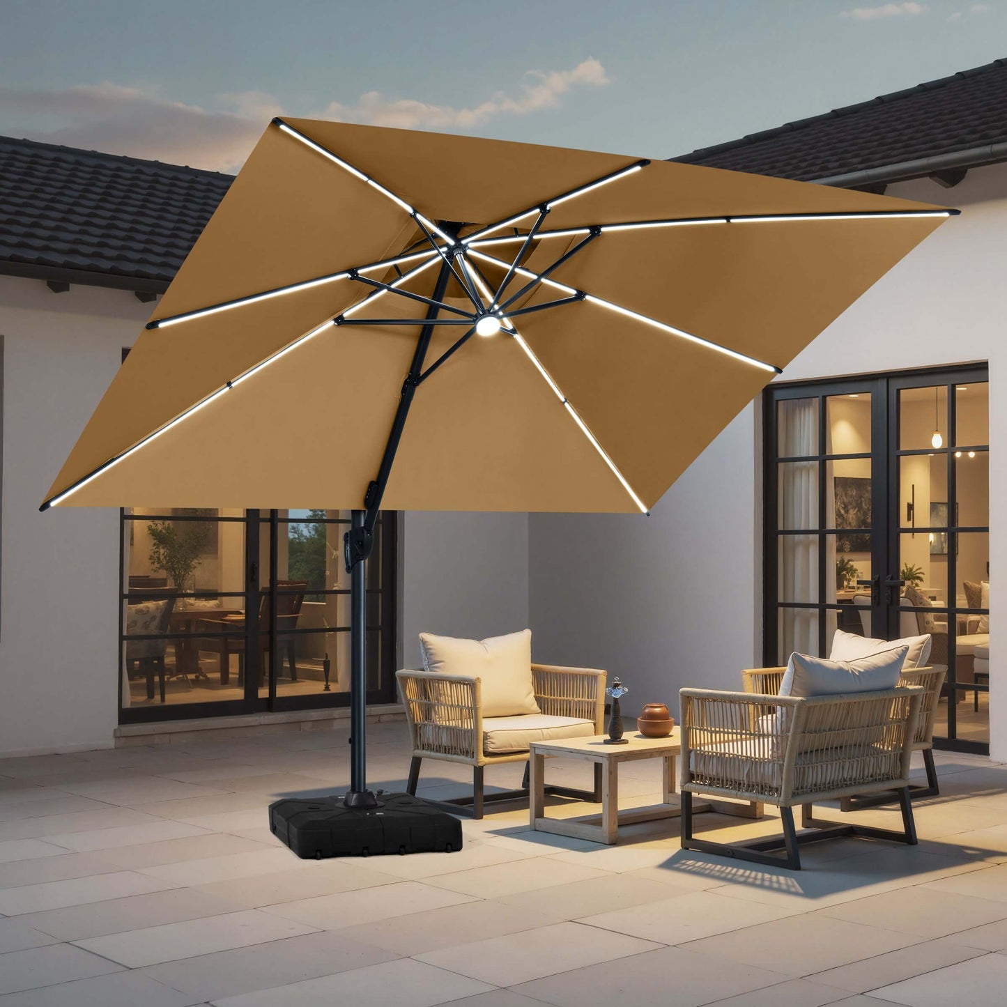Beige cantilever patio umbrella with LED lights and rolling base illuminating an evening outdoor seating area.
