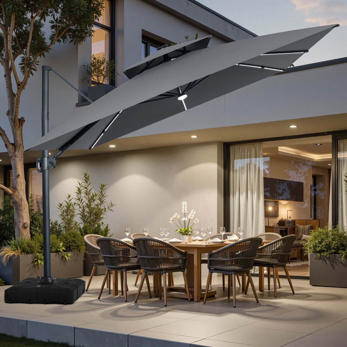 Grey LED cantilever umbrella on a wheeled base over a patio dining set at dusk.