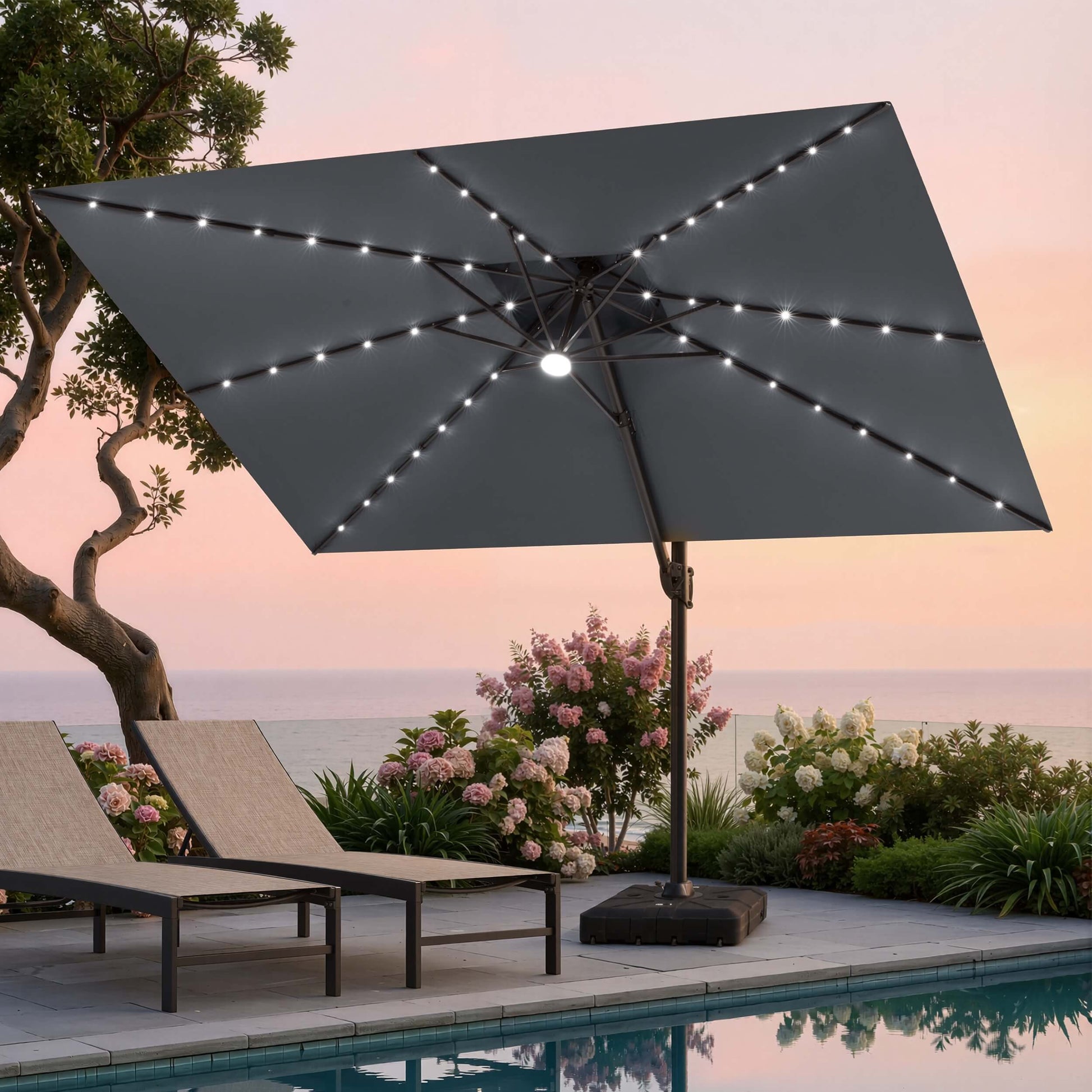 Tilted 12x9 ft grey lighted cantilever umbrella with heavy-duty base shading poolside lounge chairs at sunset