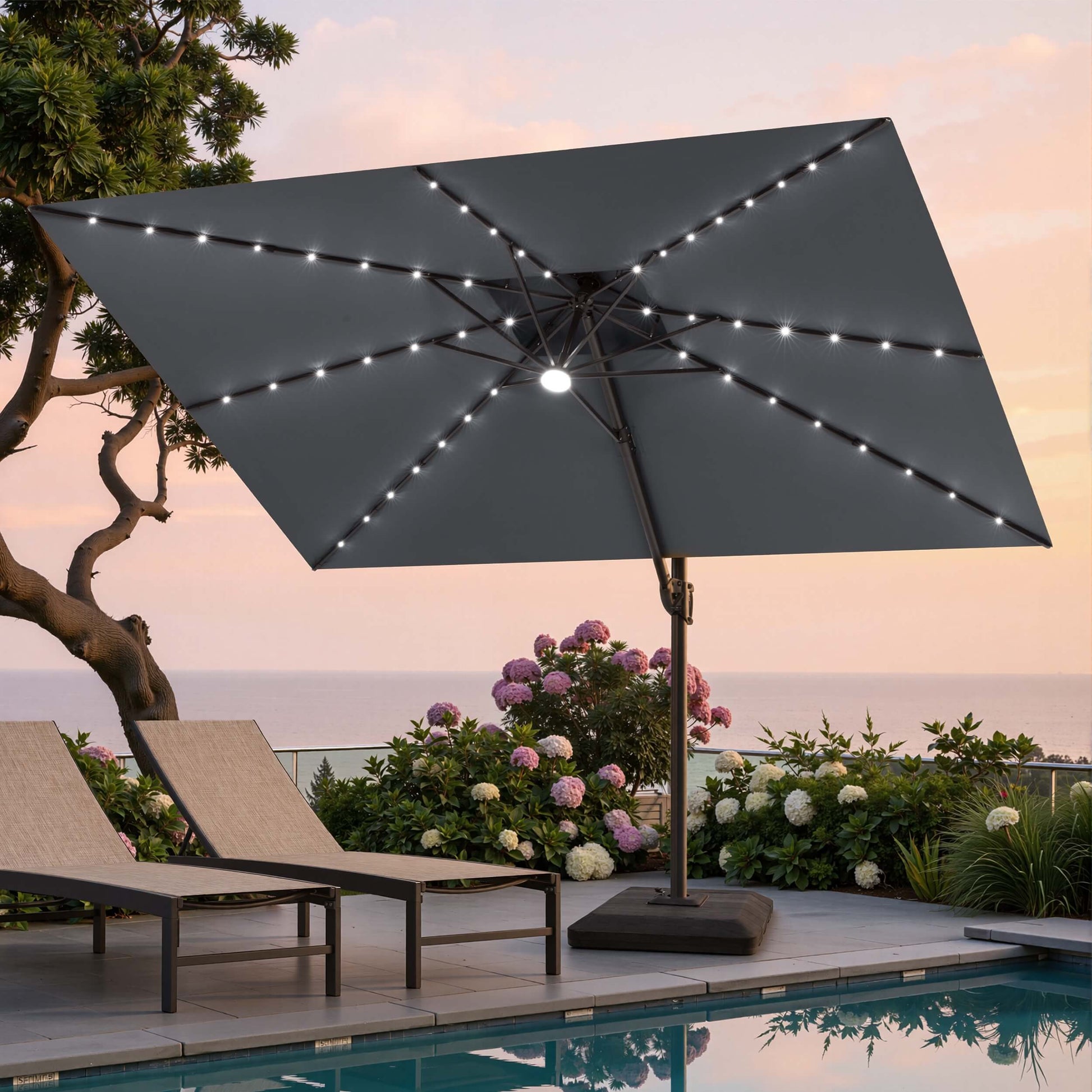 Tilted 11x9 ft grey lighted cantilever umbrella with heavy-duty base shading poolside lounge chairs at sunset ocean view