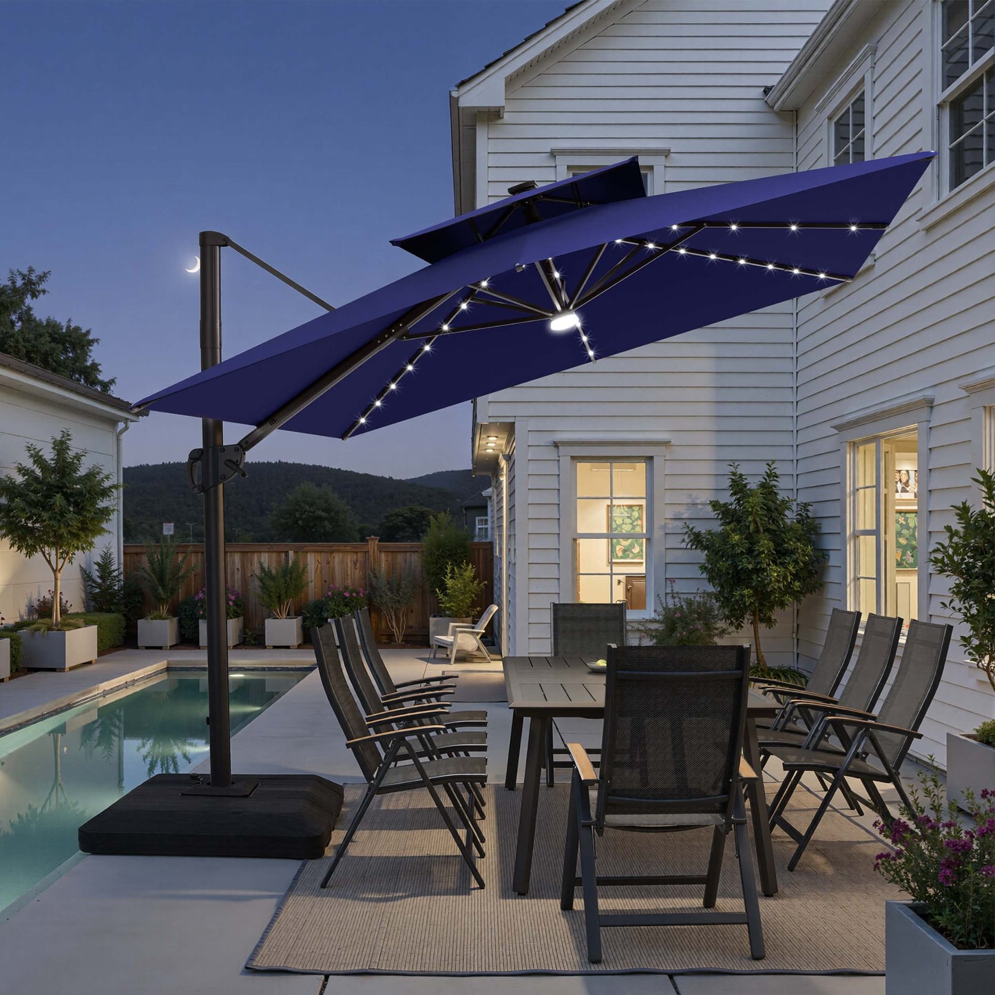 Tilted 12x9 ft navy blue lighted cantilever umbrella with low-profile base shading poolside dining set at twilight