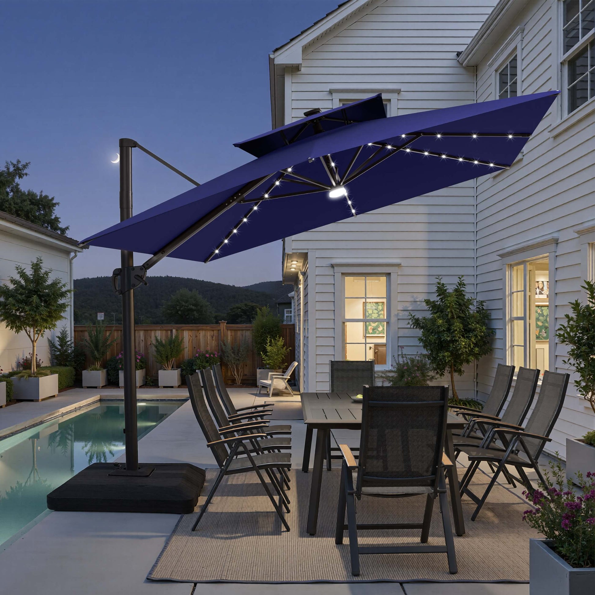 Tilted 12x9 ft navy blue lighted cantilever umbrella with low-profile base shading poolside dining set at twilight
