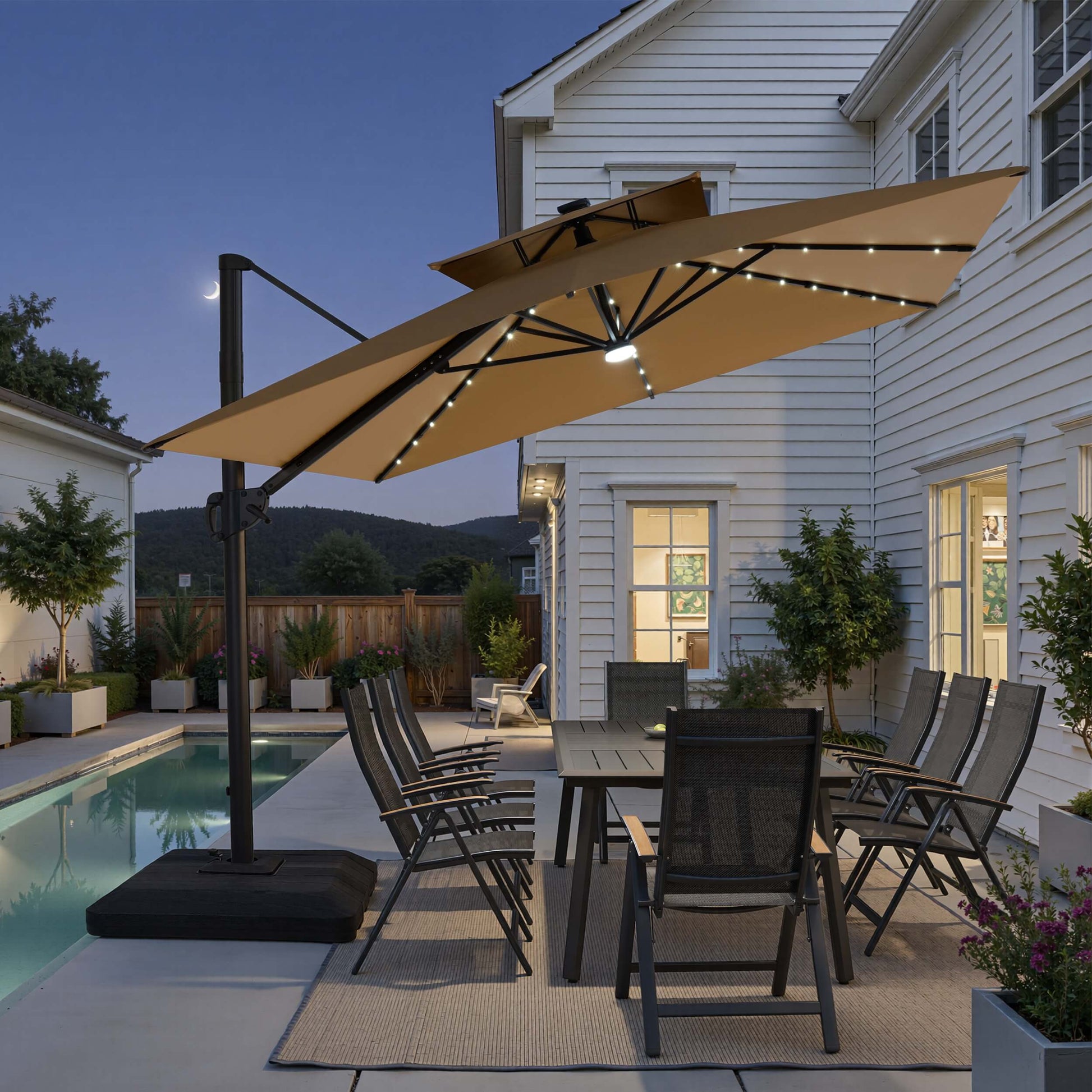 Tilted 12x9 ft beige lighted cantilever umbrella with low-profile base shading a poolside dining set at twilight