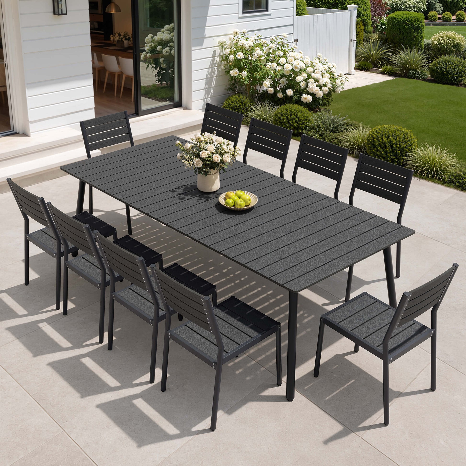 Modern black 11-piece outdoor patio dining set with large polywood table and 10 chairs on tile courtyard.