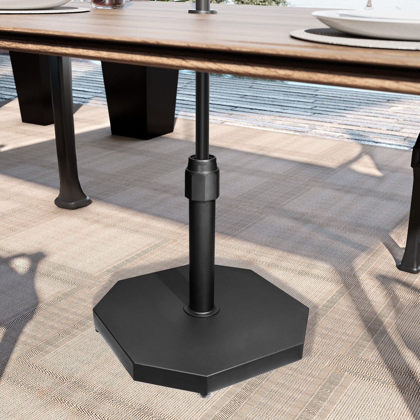 Black 40 lbs octagonal cement market umbrella base under a wooden patio dining table.